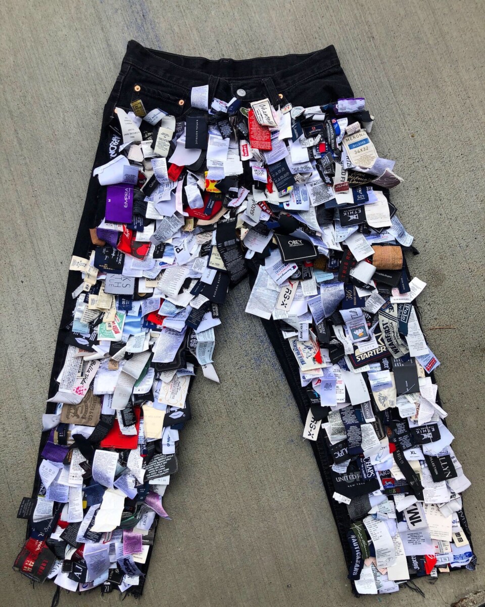 a creative use of clothing tags collected over time, arranged and attached to a pair of jeans to create a textured, visually compelling art piece